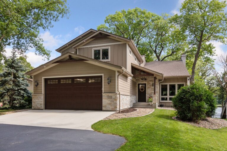 Front view of tan two-story house with stone accents, dark garage, and landscaped lawn.