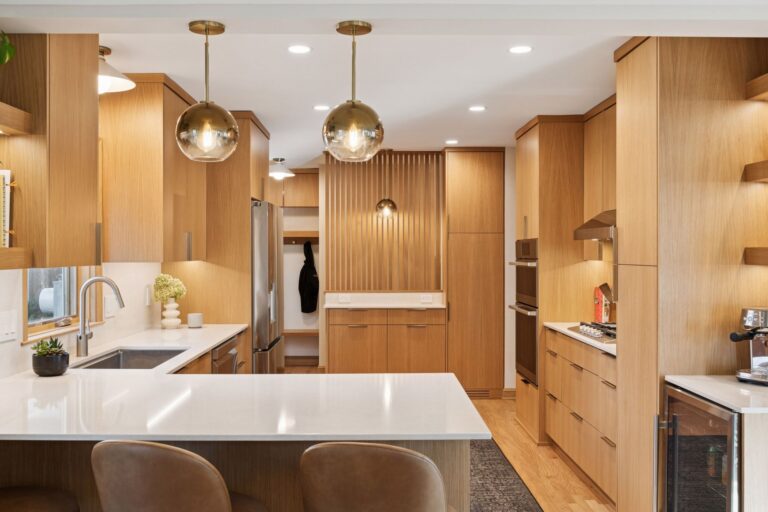 Modern kitchen with light wood cabinets, white countertops, brass pendant lights, and stainless steel appliances.