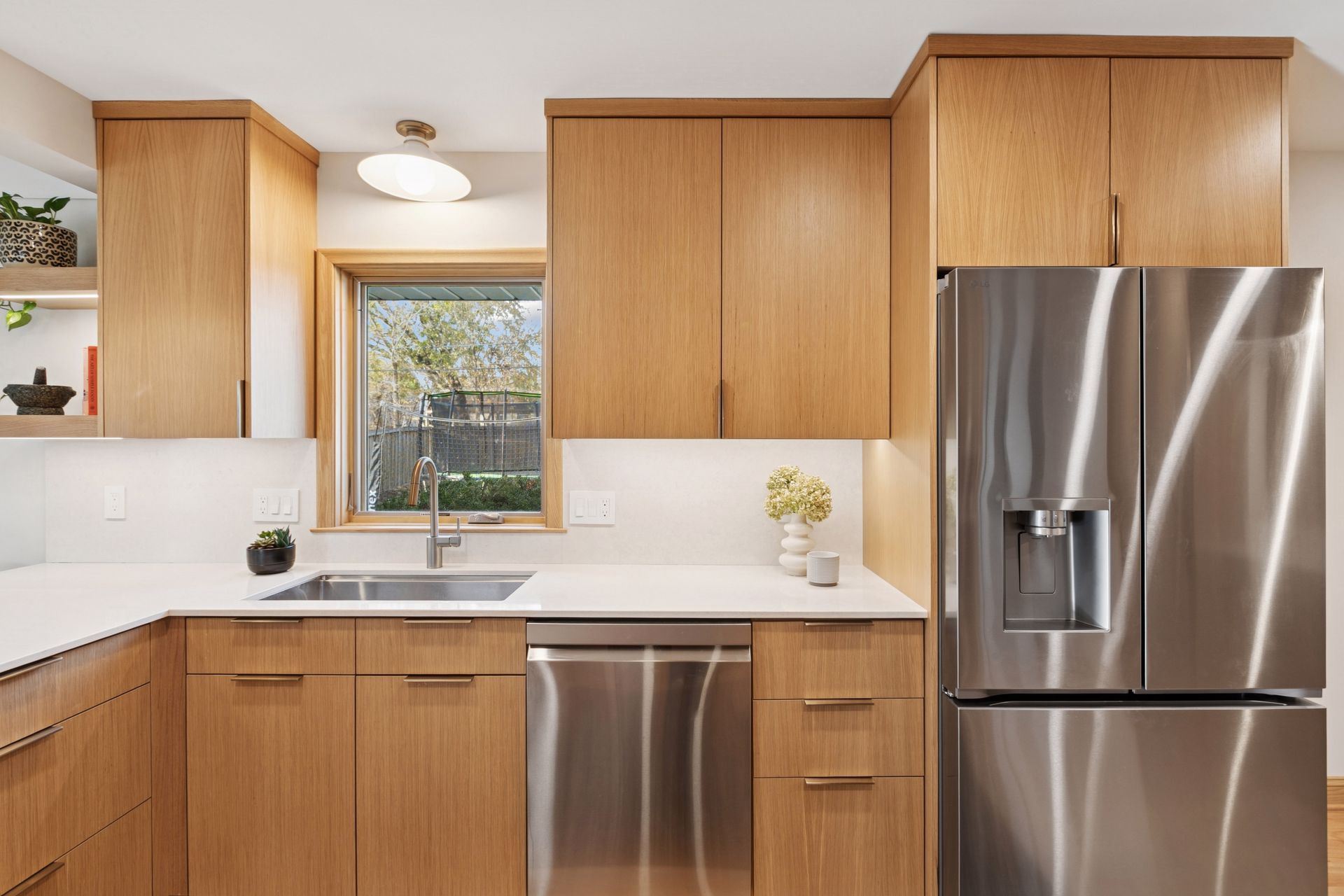 Kitchen sink area with light-wood cabinets, a stainless steel dishwasher, and a stainless steel fridge.