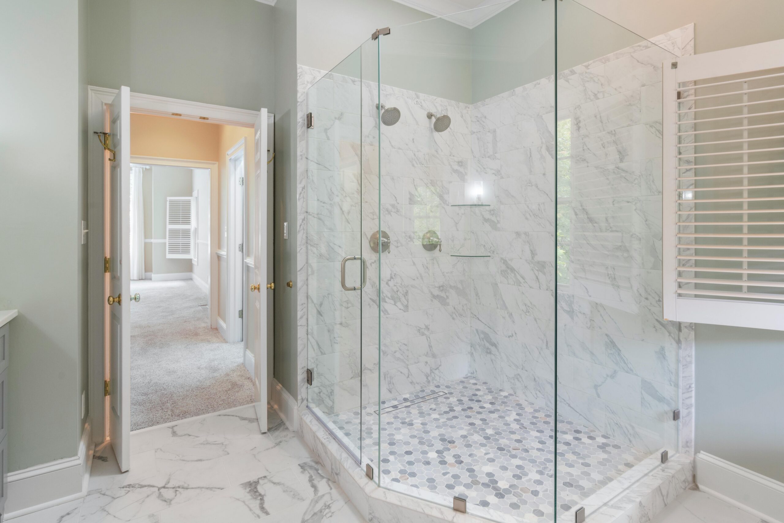 Bright primary bathroom featuring a large frameless glass walk-in shower with marble tile walls, dual showerheads, and a modern spa-like design.